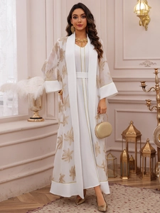 Detail of elegant white cardigan set featuring intricate golden tropical leaf embroidery