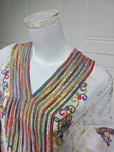 Broderie détaillée et sequins colorés sur la robe longue blanche à col en V