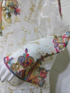 Détail de broderies à paillettes colorées et motifs en fil d'or sur robe en tulle blanc