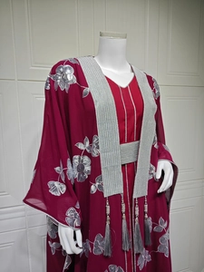 Détail de la broderie florale argentée et pompon gris sur une robe abaya rouge foncé
