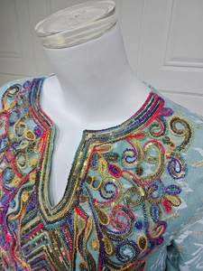 Detail of colorful floral embroidery and sequins on light blue V-neck tunic top
