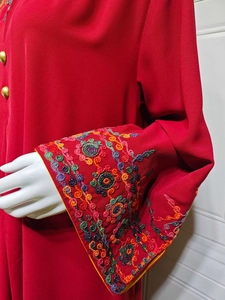 Detailed view of intricate floral embroidery on red long sleeves with gold buttons