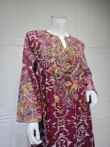 Detailed close-up of intricate gold embroidery and sequins on a burgundy kaftan neckline