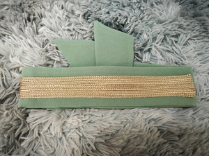Close-up of a dark green fabric waist belt with intricate gold braided lace trim detail