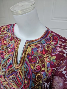Detail of colorful embroidery and sequins on a wine red ethnic mesh maxi dress neckline