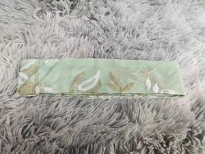 Dettaglio dell'accessorio in tessuto ricamato verde menta con motivi a foglie bianche e oro