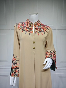 Detail of colorful bohemian embroidery and golden buttons on beige long sleeve dress