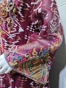 Detail of burgundy mesh dress featuring intricate white embroidery and colorful sequins