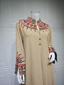 Close-up of ethnic embroidery details and gold buttons on a beige long-sleeved kaftan dress