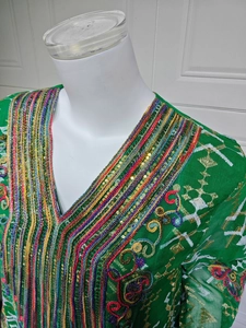 Détail macro du kaftan vert émeraude avec sequins dorés et broderie colorée sur le col V