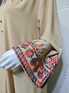 Close-up of vibrant floral embroidery on wide cuffs of a khaki long-sleeved dress