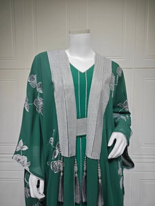 Détail de broderie florale argentée et paillettes sur une abaya vert foncé à pompons