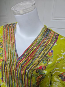 Détail du col en V avec broderie colorée complexe et paillettes sur tissu vert