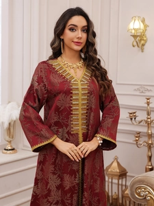 Detail of golden embroidery and beadwork on a deep red kaftan dress with leaf texture