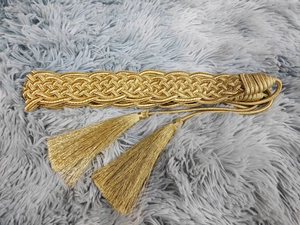 Detail of a gold braided belt with intricate woven texture and long tassels