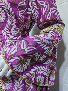 Dettaglio dei ricami intricati in oro e bianco su un abito alla moda viola