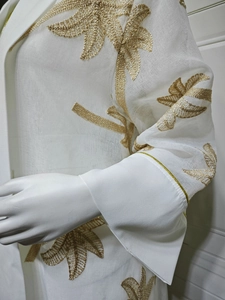 Detail of golden leaf embroidery on white semi-transparent long dress with flared cuffs