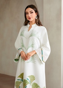 Detail of white textured dress featuring green leaf embroidery and pearl neckline accents