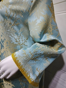 Detail of blue pleated dress with golden floral embroidery and lace crochet cuffs