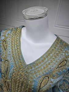 Détails de broderie dorée et perles sur le décolleté de la robe caftan en satin bleu