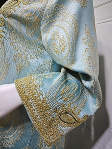 Détail du caftan bleu clair avec broderie florale dorée complexe et texture plissée