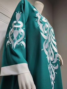 Detail of white embroidery patterns and color blocking on dark green kaftan dress