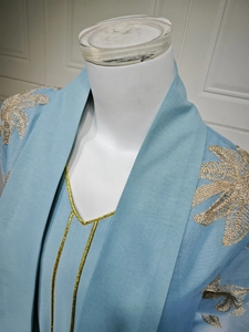 Detail of light blue dress with elegant gold leaf embroidery and V-neckline design