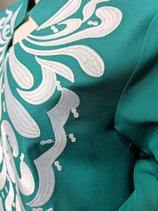 Detail of white embroidery on peacock green fabric showing intricate floral stitching texture