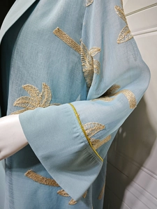 Detail of light blue robe featuring intricate gold leaf embroidery and wide cuffs