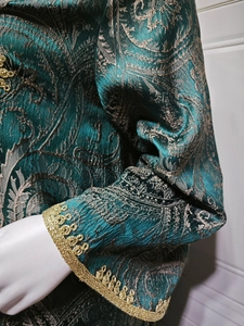 Detail of dark green jacquard fabric with golden lace cuffs and paisley embroidery