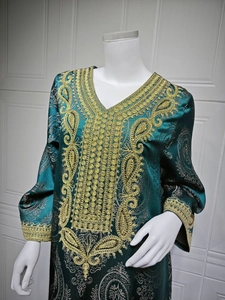 Détail de broderie paisley dorée sur robe caftan vert foncé avec texture satinée