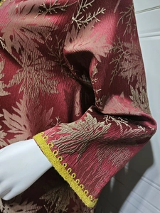 Close-up of wine red pleated dress sleeve with golden maple embroidery and yellow lace