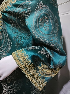 Détail de broderies dorées sur la manche d'un caftan vert foncé en tissu jacquard