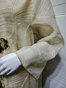 Dettaglio ricamo a foglia e bordo dorato su abito lungo etnico in tulle beige.