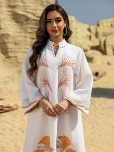 Detail of white long sleeve dress featuring intricate orange beadwork and textured fabric