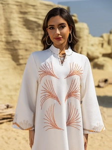 Close-up of white long sleeve dress featuring silver bead collar and ethnic orange embroidery