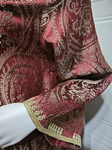 Detail of red jacquard fabric with gold paisley embroidery and woven cuffs on evening kaftan
