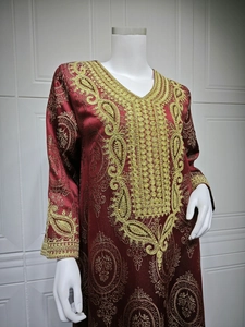 Gros plan de la broderie dorée et du jacquard paisley sur robe caftan rouge foncé