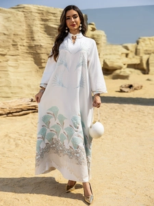 Detailed view of white abaya with intricate blue and gold feather embroidery in desert