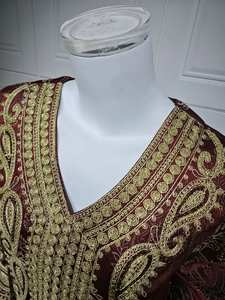 Détail de broderie dorée sur le col en V d'une robe caftan en jacquard bordeaux luxueuse