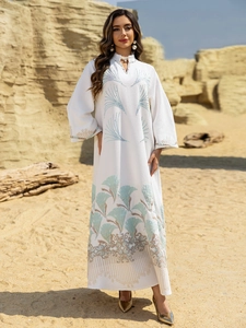 Detail of white V-neck Abaya dress featuring blue palm leaf embroidery and fringe hem