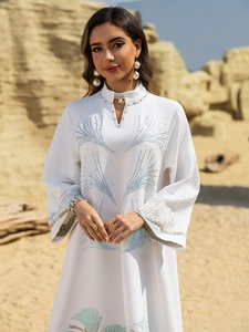 Detailed close-up of the white abaya dress featuring blue floral embroidery and pearl trim