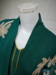 Detail of emerald green kaftan with intricate gold leaf embroidery on shoulders and neck
