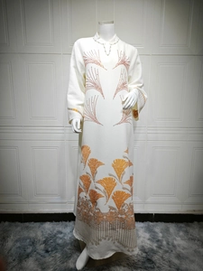 Detail of white long-sleeved dress with intricate orange and gold floral embroidery