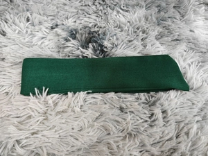 Detail of dark green fabric belt accessory with textured stitching on grey faux fur