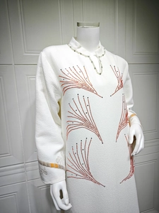 Detail of white textured fabric with orange rhinestones and pearl collar accent
