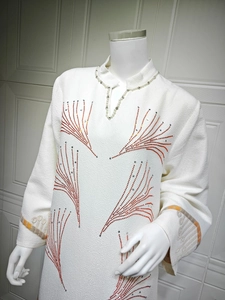 Detail of white jacquard dress with orange rhinestone patterns and pearl V-neckline
