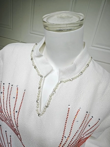 Close-up of white textured long sleeve dress featuring pearl and rhinestone V-neckline detail