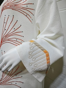 Detailed view of white crepe fabric with intricate rhinestone pattern and woven cuffs