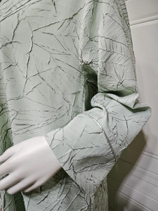 Detailed close-up of light green jacquard fabric with leaf-like pleated textures and silver trim